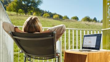 A person relaxing on a chair with a laptop on a wooden table, overlooking a grassy field.