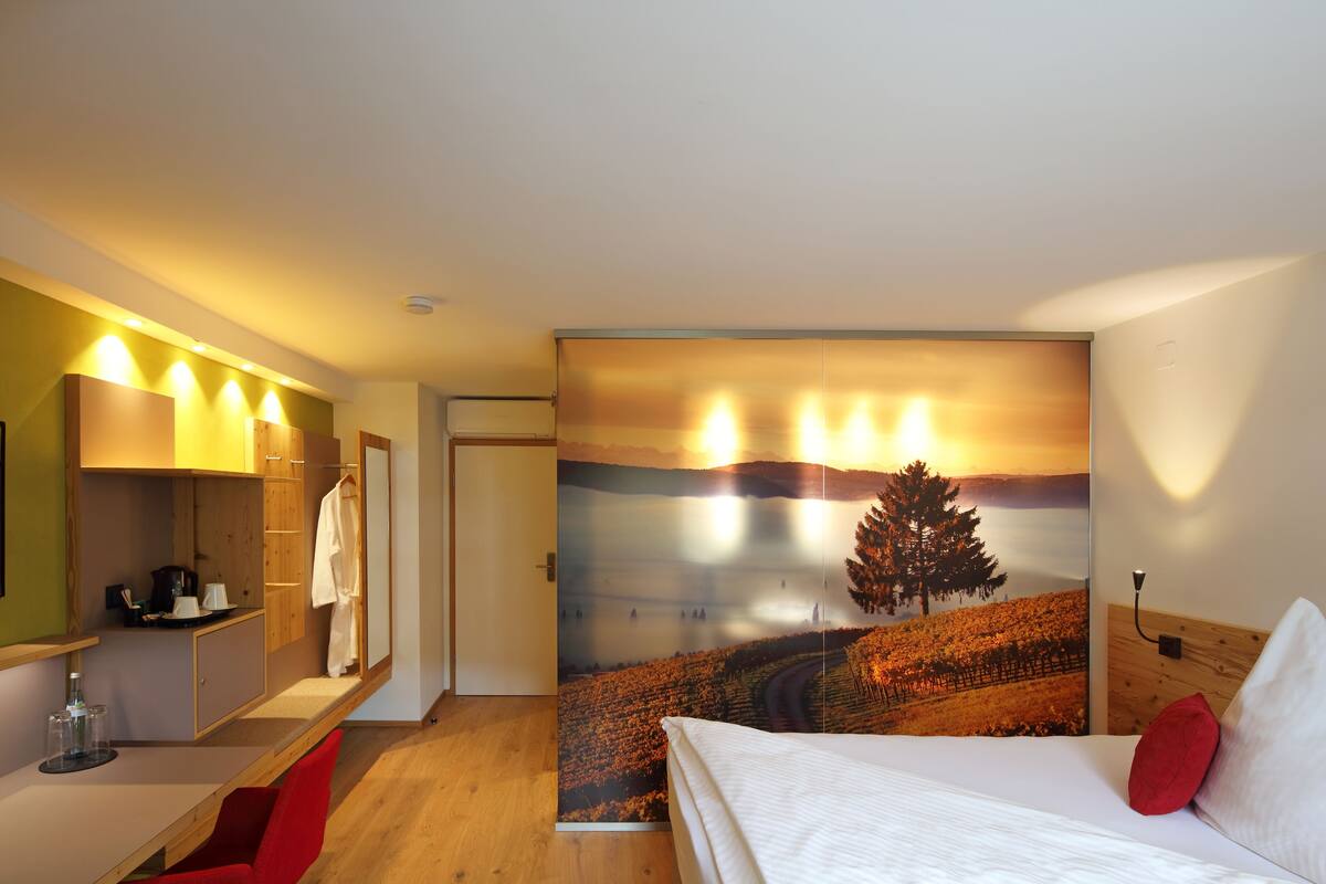 A hotel room with a bed, a desk, a wardrobe, and a large wall mural.