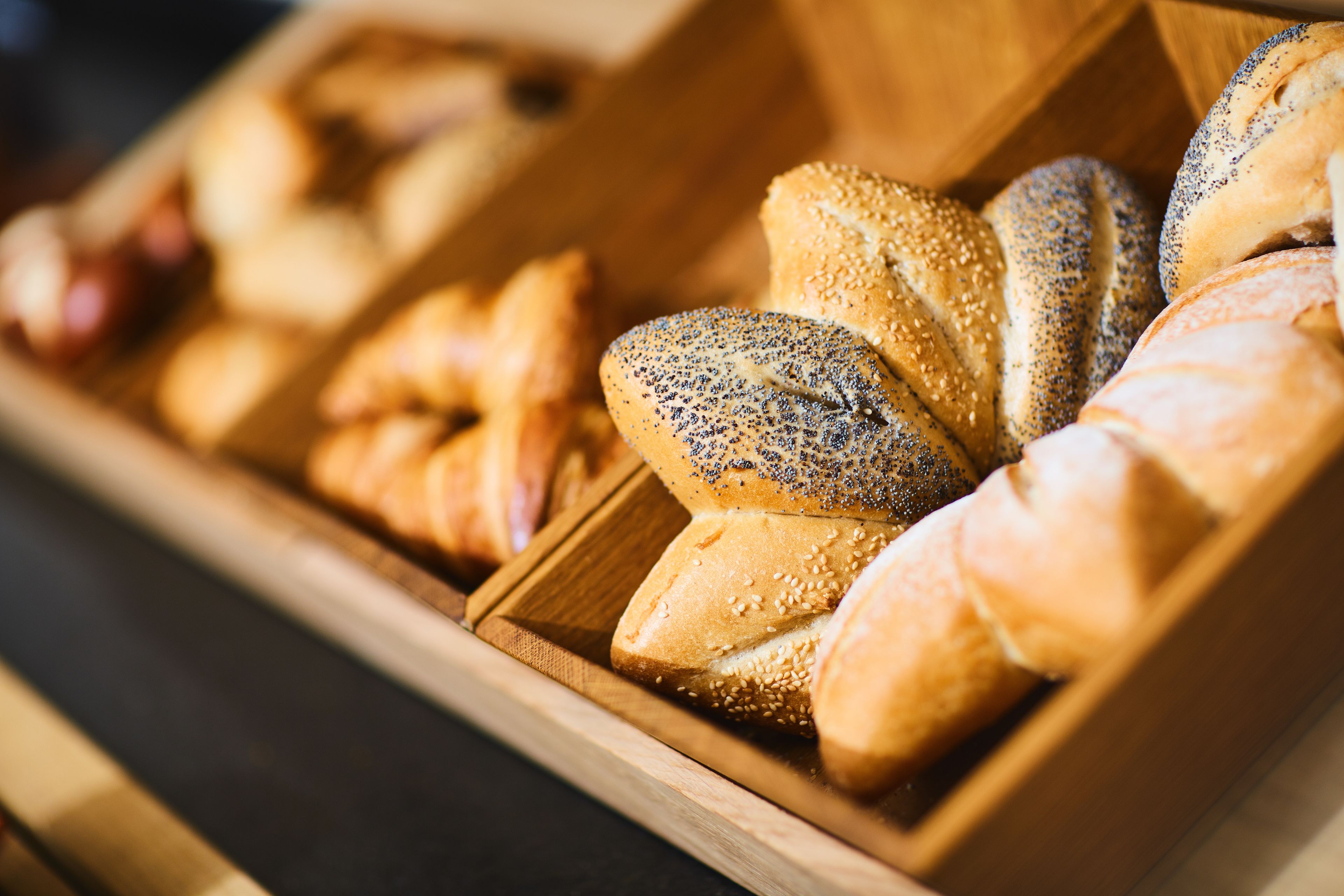 A wooden bread display case with various types of bread, including poppy seed and sesame seed varieties.