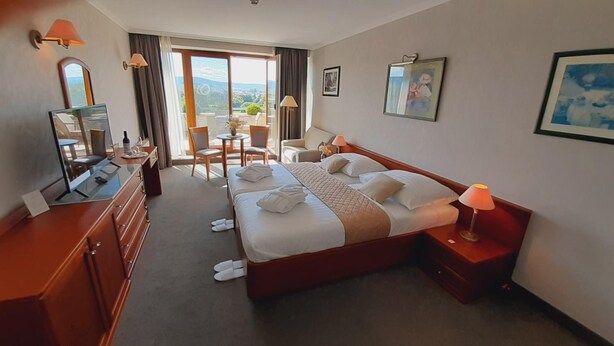 A hotel room with a bed, bedside tables, a desk, a chair, and a view of the outdoors. - Rosengarten Hotel Restaurant (Sopron)
