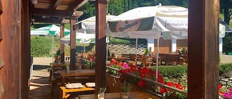 An outdoor seating area with wooden tables and chairs, surrounded by flower beds and umbrellas.