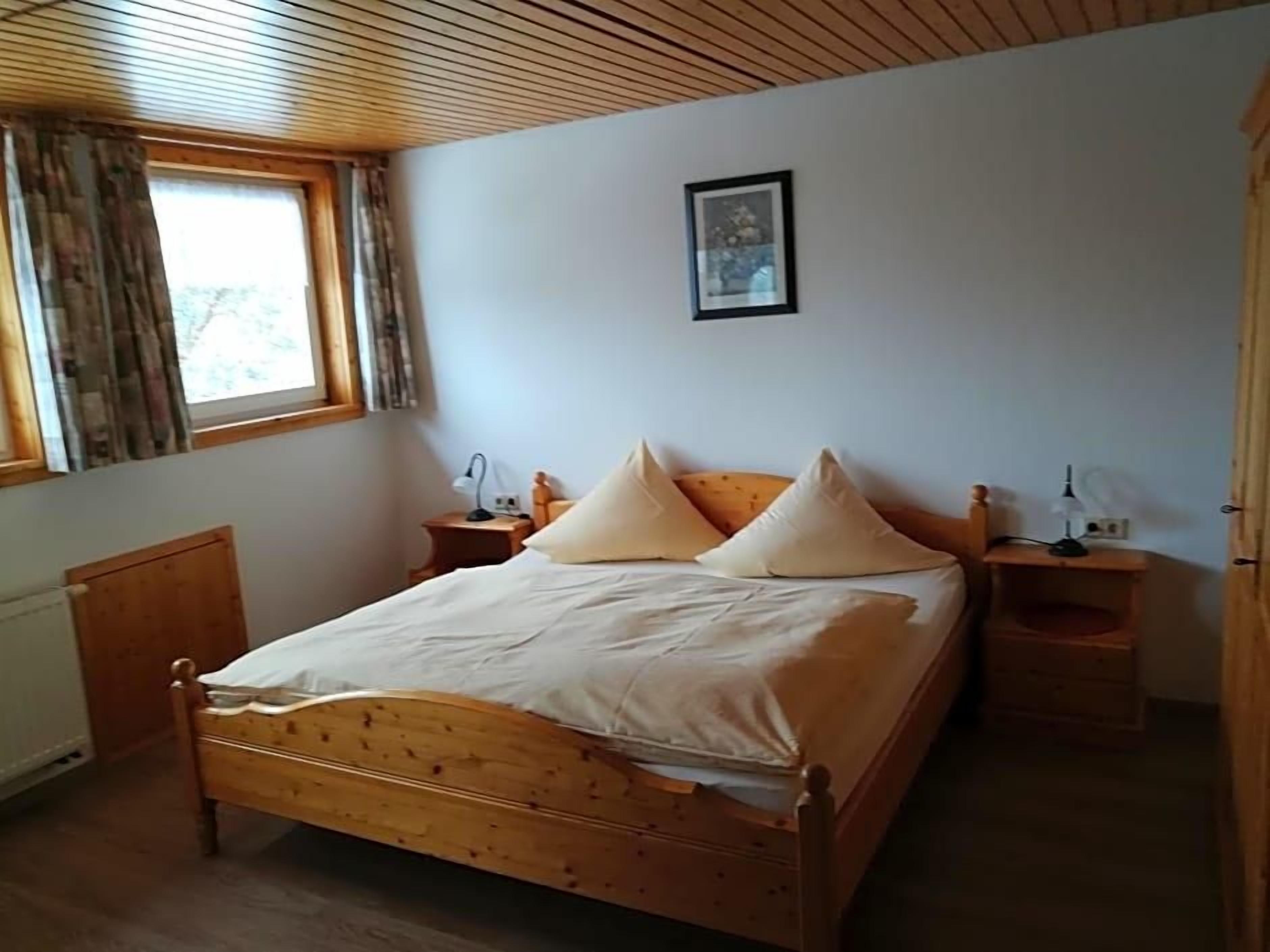 A bedroom with a wooden bed, two bedside tables, a window with curtains, and a framed picture on the wall.