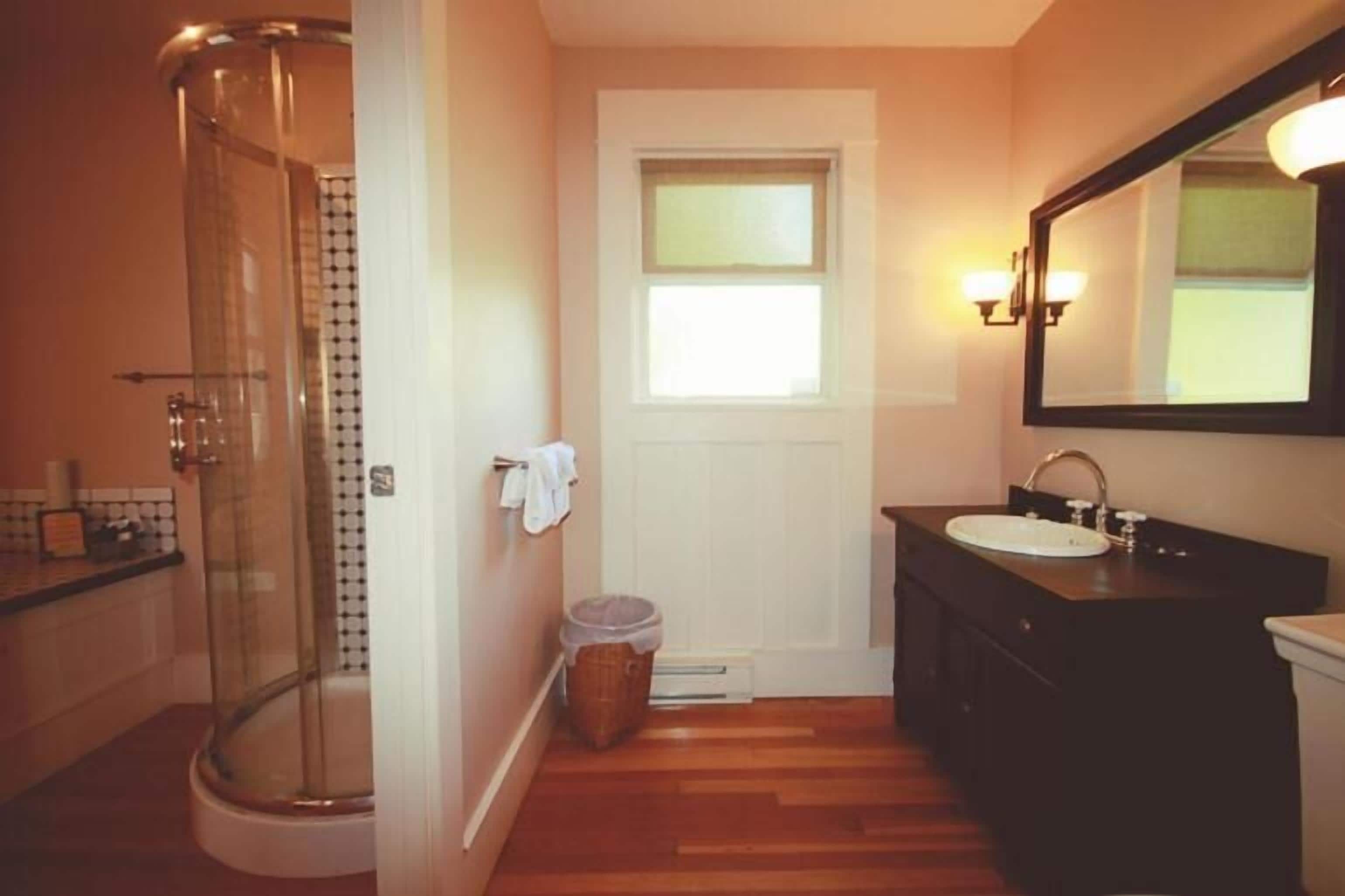 Une salle de bain avec une douche à parois de verre, une porte blanche, une fenêtre, un lavabo et un miroir.