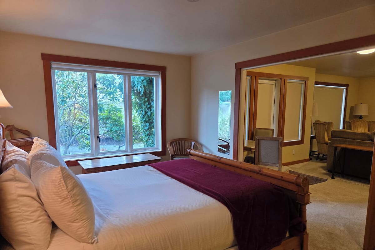 A bedroom with a large bed, a window with a view of trees, a desk, and a chair.