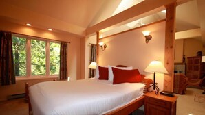 A large bed with white linens and red pillows, wooden headboard, two bedside lamps, and a view of trees through a window. - The Catherine St Guesthouse (Victoria)