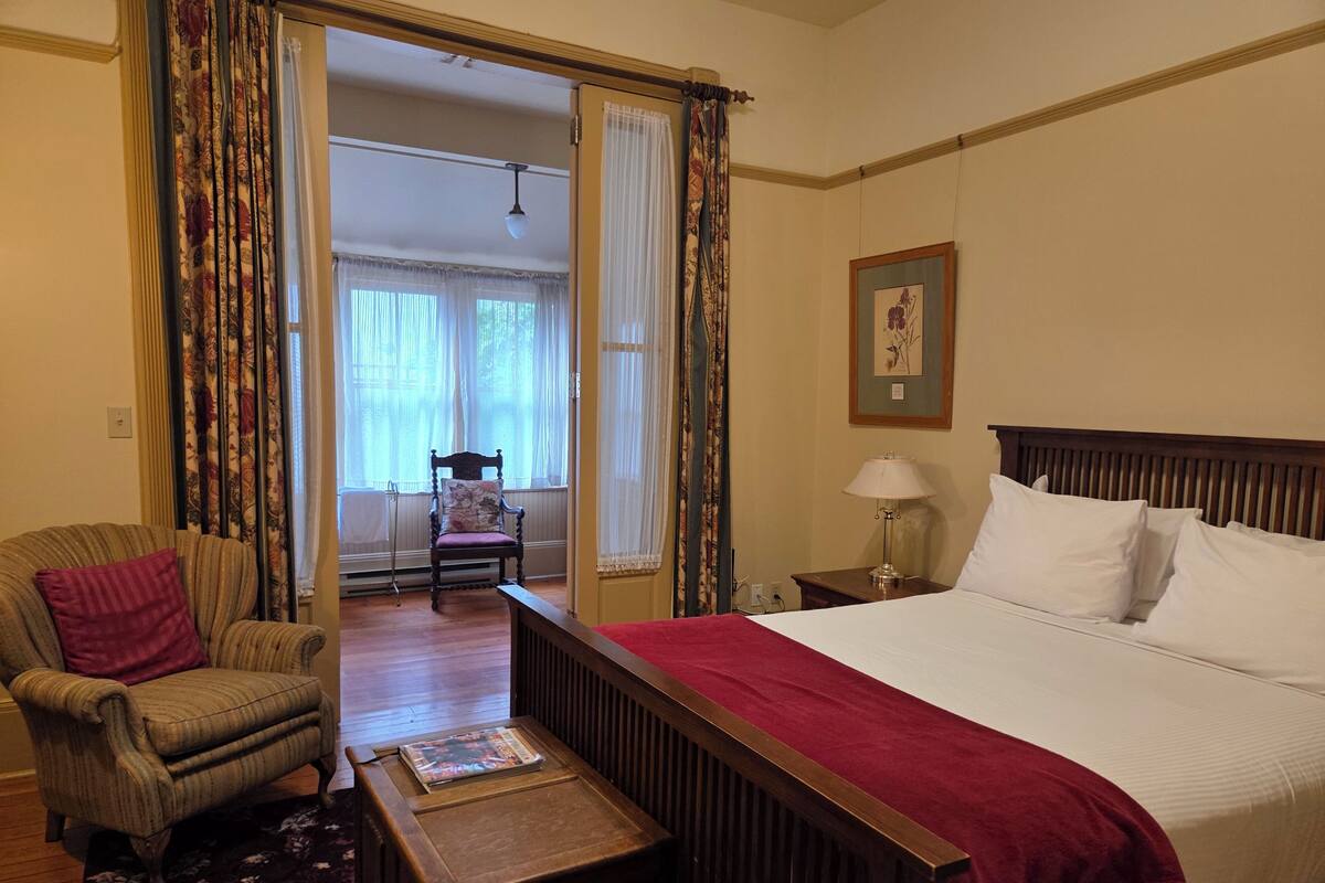 A bedroom with a large bed, a wooden nightstand, a chair, and a small table.