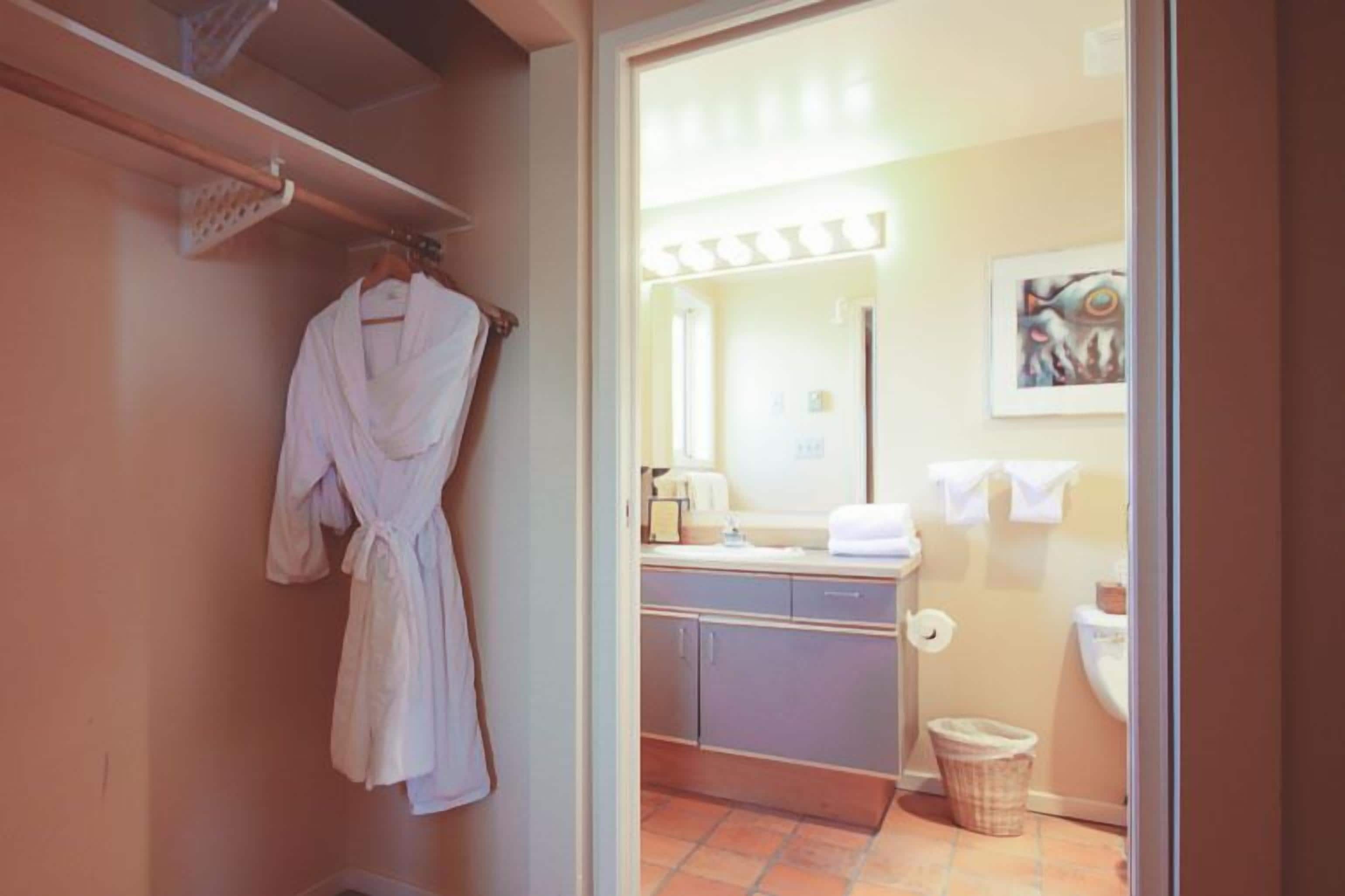 Un baño con una bata colgada en un perchero, un lavabo con espejo y un cubo de basura.