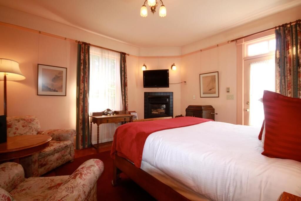 A hotel room with a large bed, a television mounted on the wall, a desk with a chair, and a fireplace.