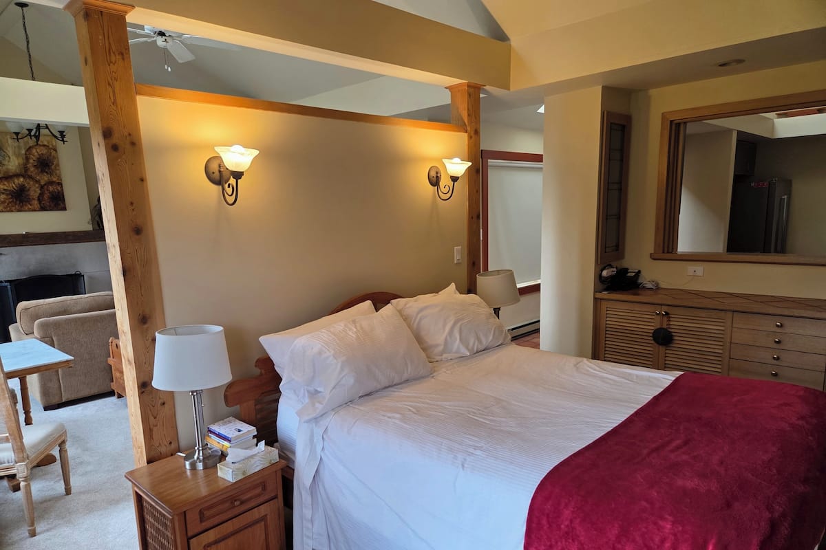 A bedroom with a large bed, wooden headboard, bedside tables, a desk, and a chair.