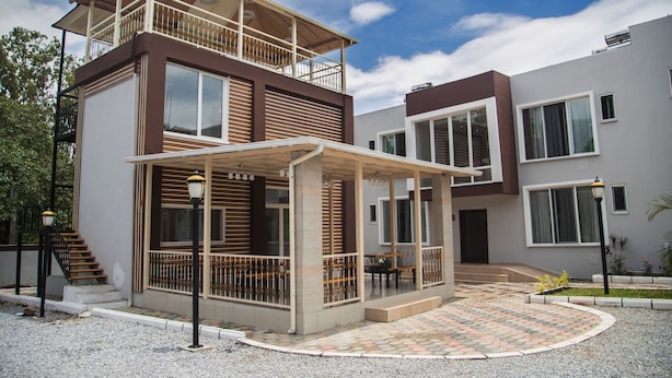A two-story building with a balcony, a covered outdoor seating area, and a paved courtyard. - Troy Serviced Apartments (Lusaka)