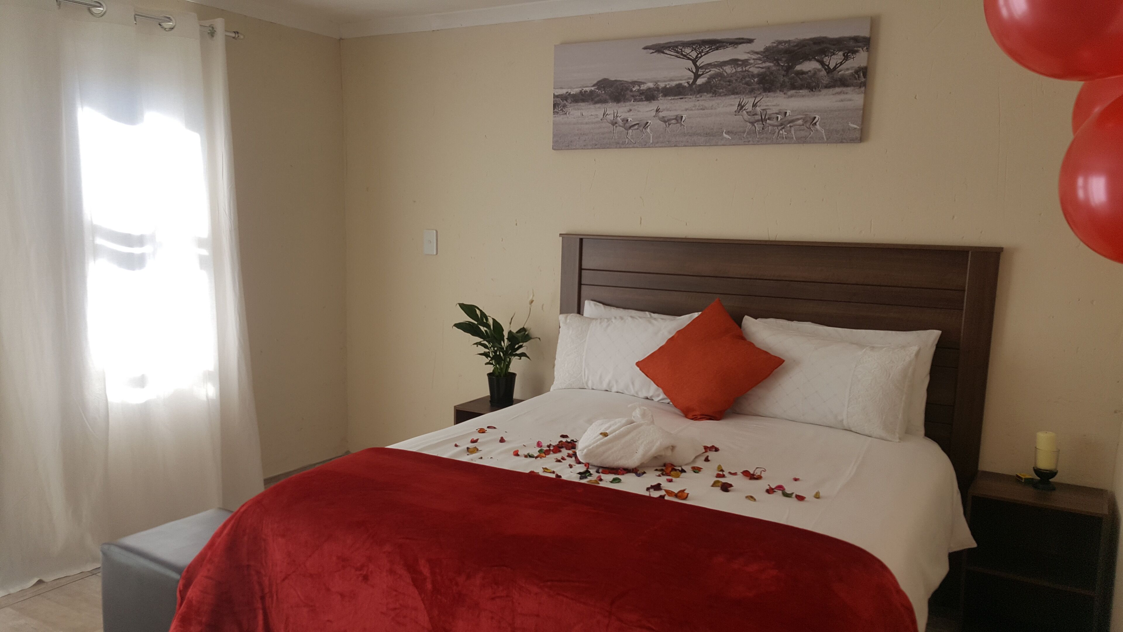 Hotelkamer met een bed, nachtkastje, een bloempot, een schilderij aan de muur en een raam met gordijnen.