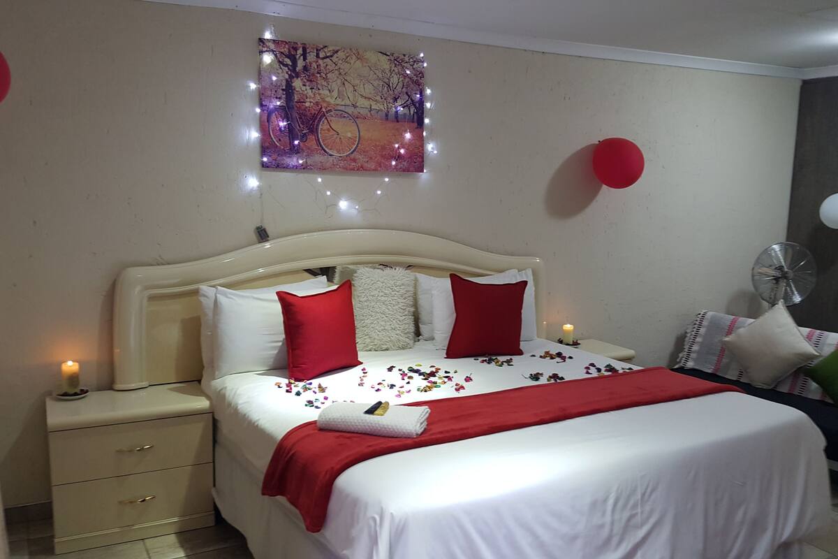 Een netjes ingerichte slaapkamer met een bed, nachtkastjes, een kunstwerk aan de muur en een plafondventilator.