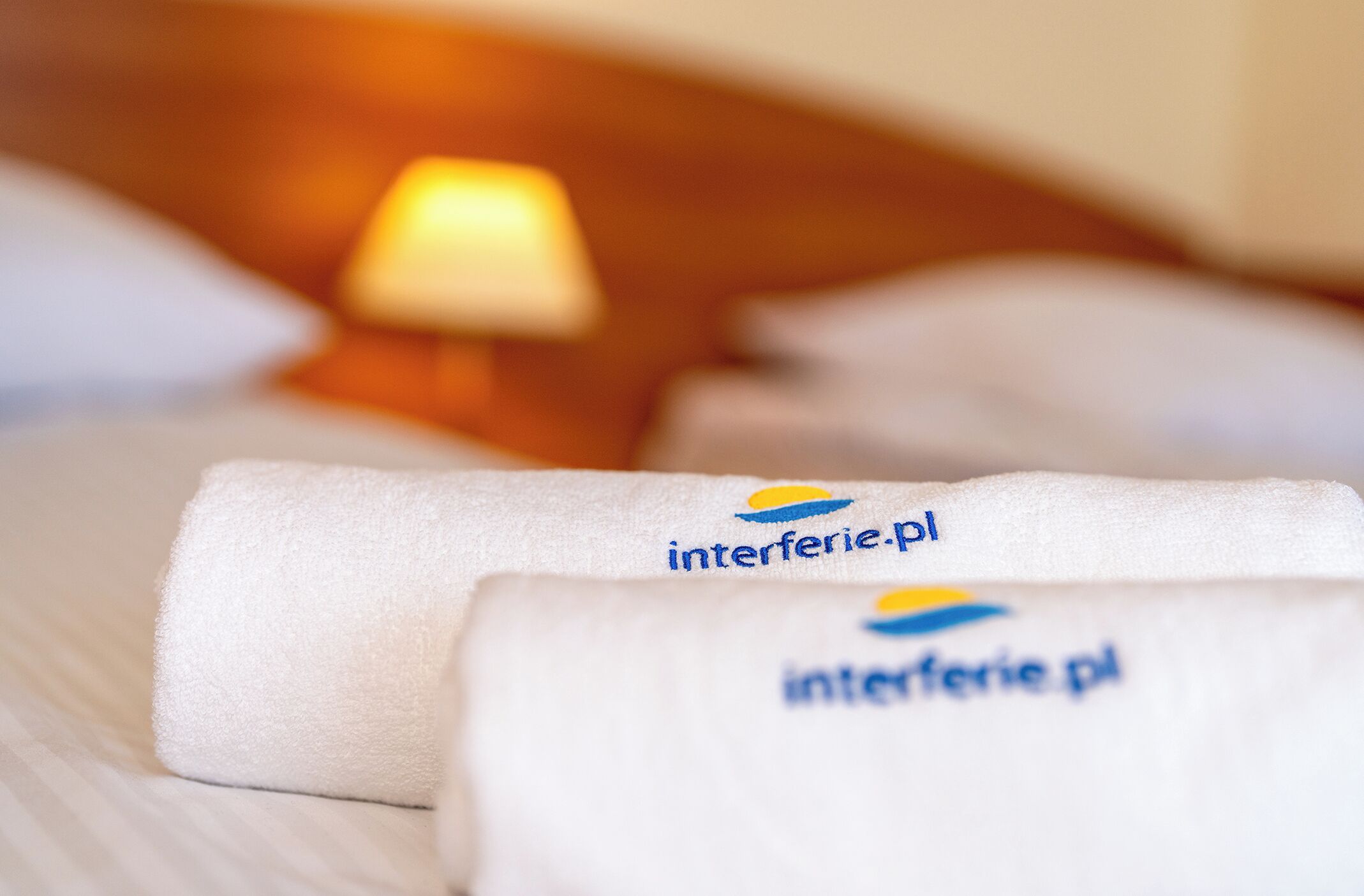 Cama bem arrumada com lençóis brancos e um logotipo nos travesseiros.