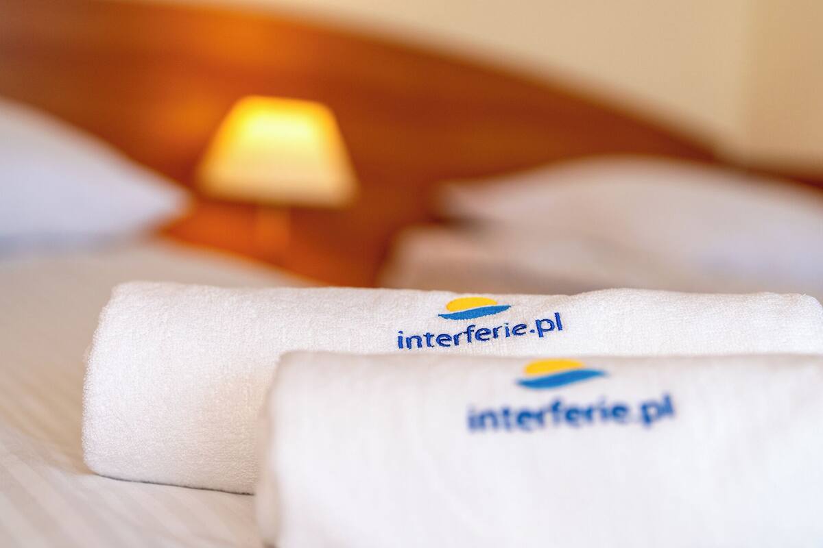 A neatly made bed with white linens and a logo on the pillows.