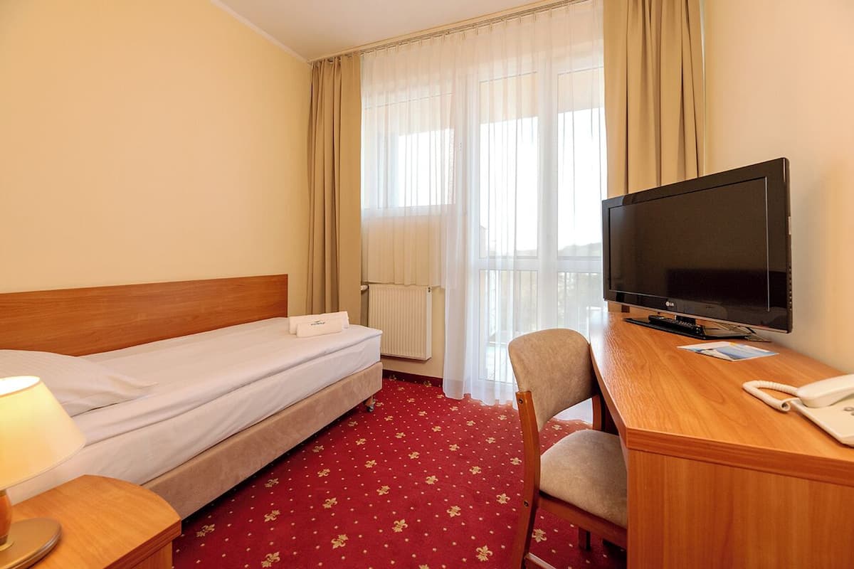 A hotel room with a single bed, a desk with a television, a chair, and a telephone.