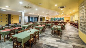 Un amplio comedor con múltiples mesas y sillas, piso de mármol y techo amarillo con iluminación empotrada.