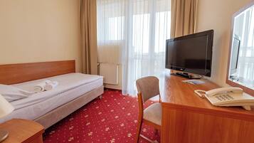 A hotel room with a bed, a desk with a TV, a chair, a phone, and a window with curtains.