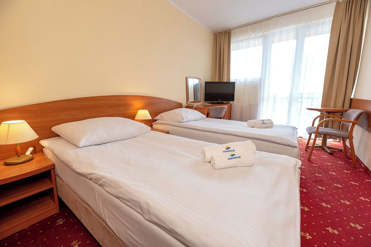 A hotel room with two beds, a TV, a desk, and a chair.