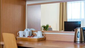 Habitación de hotel con un escritorio de madera, una bandeja con tazas y una tetera, y un espejo grande que refleja la habitación.