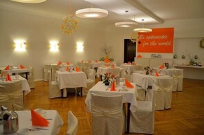 Un salón de banquetes con mesas redondas, manteles blancos y servilletas naranjas.