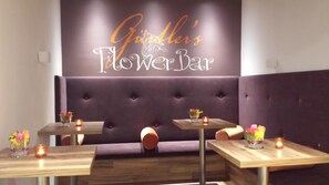 Interior de restaurante con letrero que dice 'Flower Bar', asientos acolchados y mesas con velas.