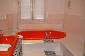 A bathroom with a red bathtub, a white sink, and a window with blinds. - Stadthotel Gürtler (Amstetten)