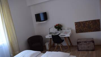 Ein Hotelzimmer mit einem Bett, einem Schreibtisch mit Stuhl, einem Fernseher, einem kleinen Tisch mit Blumenvase und einem Gemälde an der Wand.