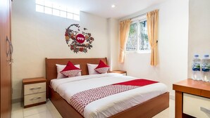 A hotel room with a bed, a nightstand, a desk with water bottles, a window with curtains, and a wall decoration. - Stadthotel Gürtler (Amstetten)