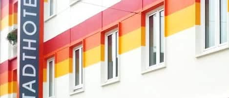 Un hotel de varios pisos con fachada roja y blanca, numerosas ventanas y una entrada visible.