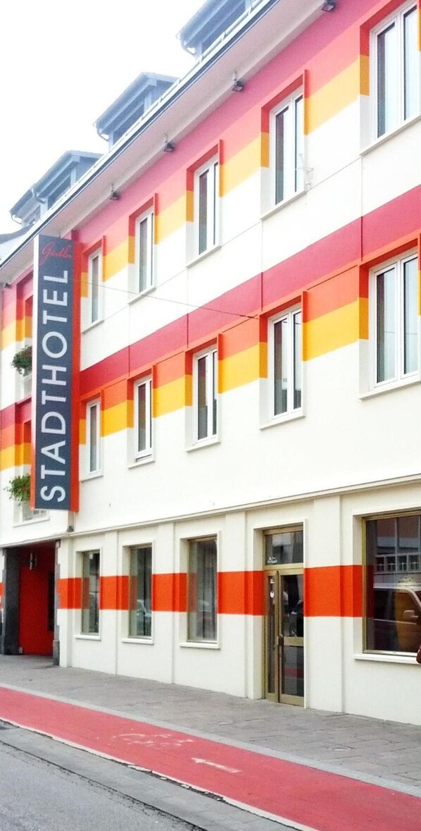 Un hotel de varios pisos con fachada roja y blanca, numerosas ventanas y una entrada visible.