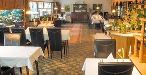 A restaurant with tables and chairs, a tiled floor, and a counter with a display of flowers. - Klosterhof (Wehr)