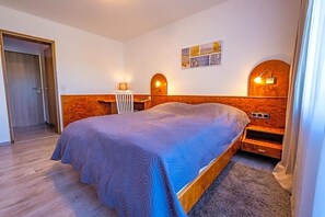 A bedroom with a bed, bedside tables, a lamp, and a wall-mounted light fixture. - Klosterhof (Wehr)