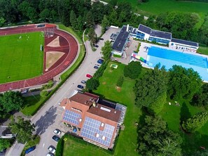 An aerial view of a sports complex with a running track, a swimming pool, and a building with solar panels. - Klosterhof (Wehr)