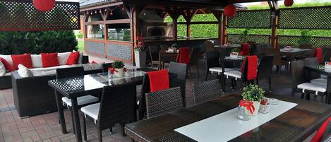 Un patio al aire libre con mobiliario de mimbre, cojines rojos y suelo de ladrillo.