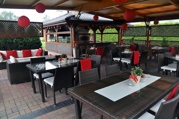 An outdoor patio with wicker furniture, red cushions, and a brick floor.