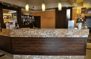 A reception desk with a marble top and wooden paneling, a wall-mounted sign reading 'Recepça', and a display of bottled beverages. - Ahotel (Czechowice-Dziedzice)