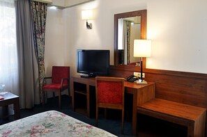 A hotel room with a bed, a desk with a television, two chairs, a telephone, and a mirror.