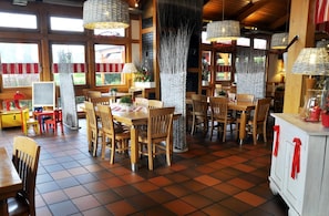 A restaurant with wooden tables and chairs, hanging woven light fixtures, and large windows.