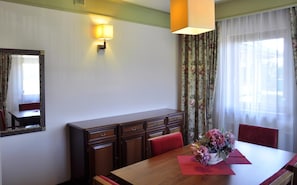 A hotel room with a wooden dining table, red chairs, a floral centerpiece, a mirror, and a wall-mounted lamp.