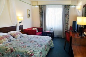 A hotel room with a bed, a desk, a chair, a television, and a window with curtains.