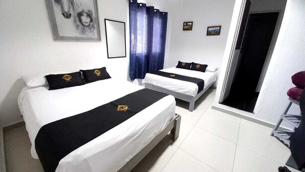 A hotel room with two beds, a large window with blue curtains, a framed picture on the wall, and a door leading to another room. - RCH Suite (Mexico City)