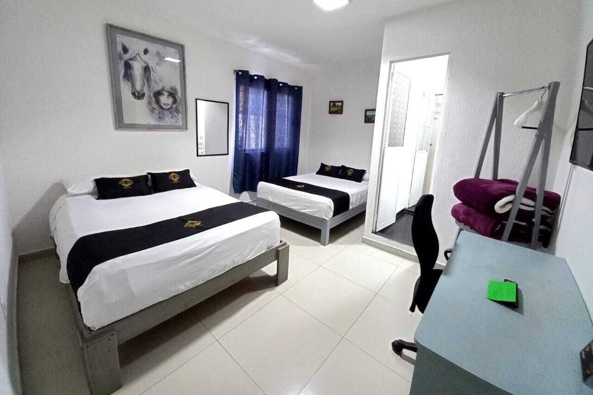 A hotel room with two beds, a desk, a chair, a mirror, and a door.