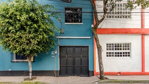 A building with a blue facade, a black gate, and a tree in front. - RCH Suite (Mexico City)