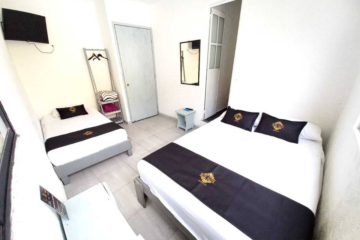 A hotel room with two beds, a small table, a mirror, and a TV on the wall.