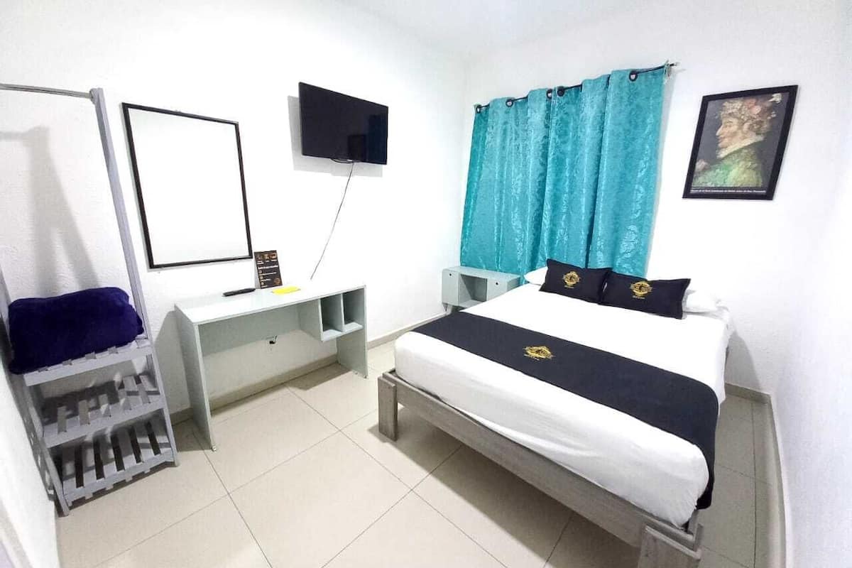 A hotel room with a bed, a desk, a chair, a TV, and a window with curtains.
