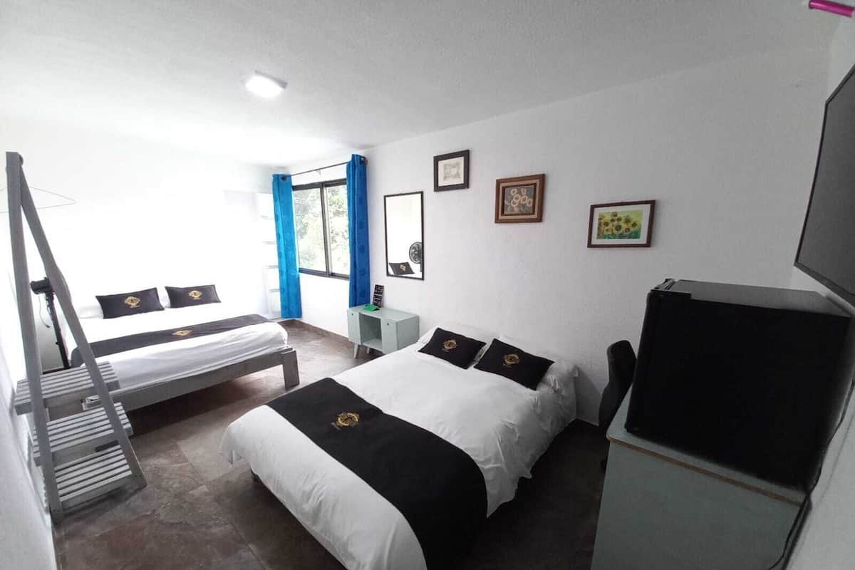 A hotel room with two beds, a desk, a TV, and a window with curtains.