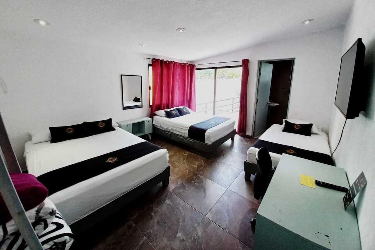 A hotel room with two beds, a desk, a TV, and a window with curtains.