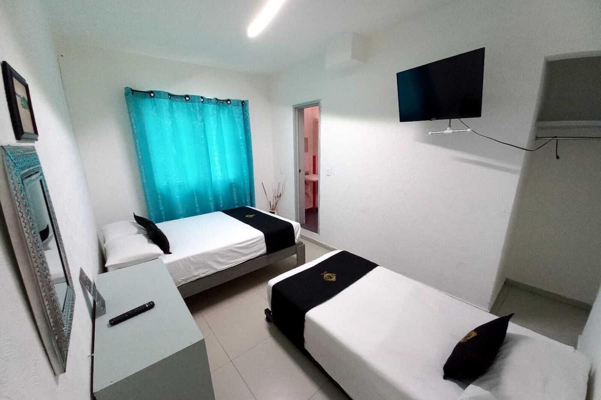 A small, clean room with two single beds, a desk, a flat-screen TV, and a window with curtains.
