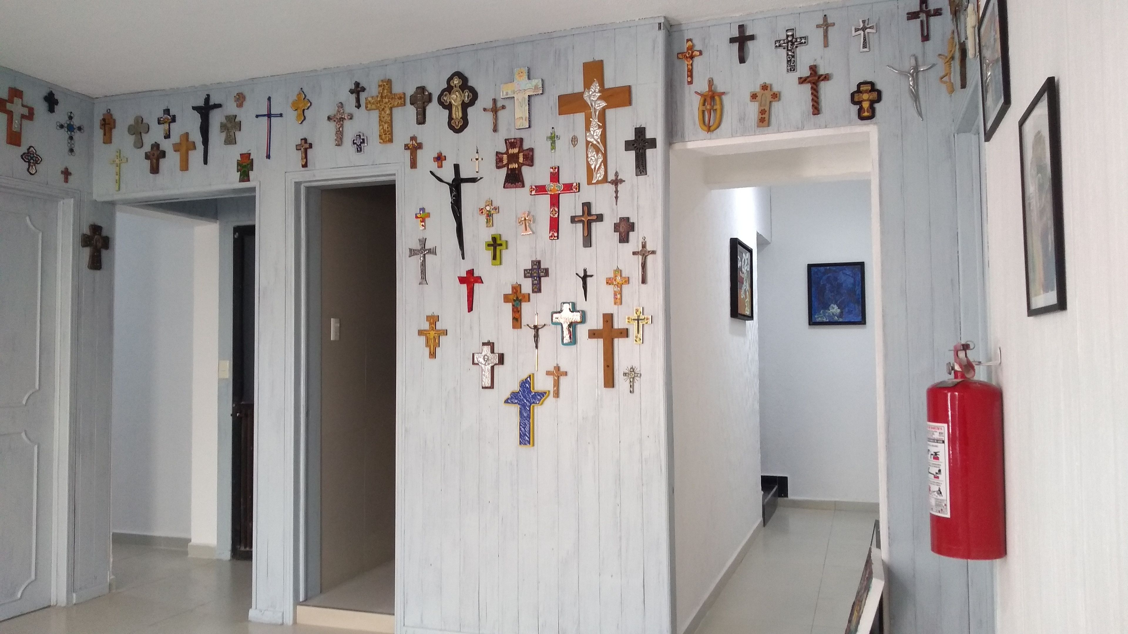 A hallway with numerous religious symbols on the walls and a fire extinguisher on the right.