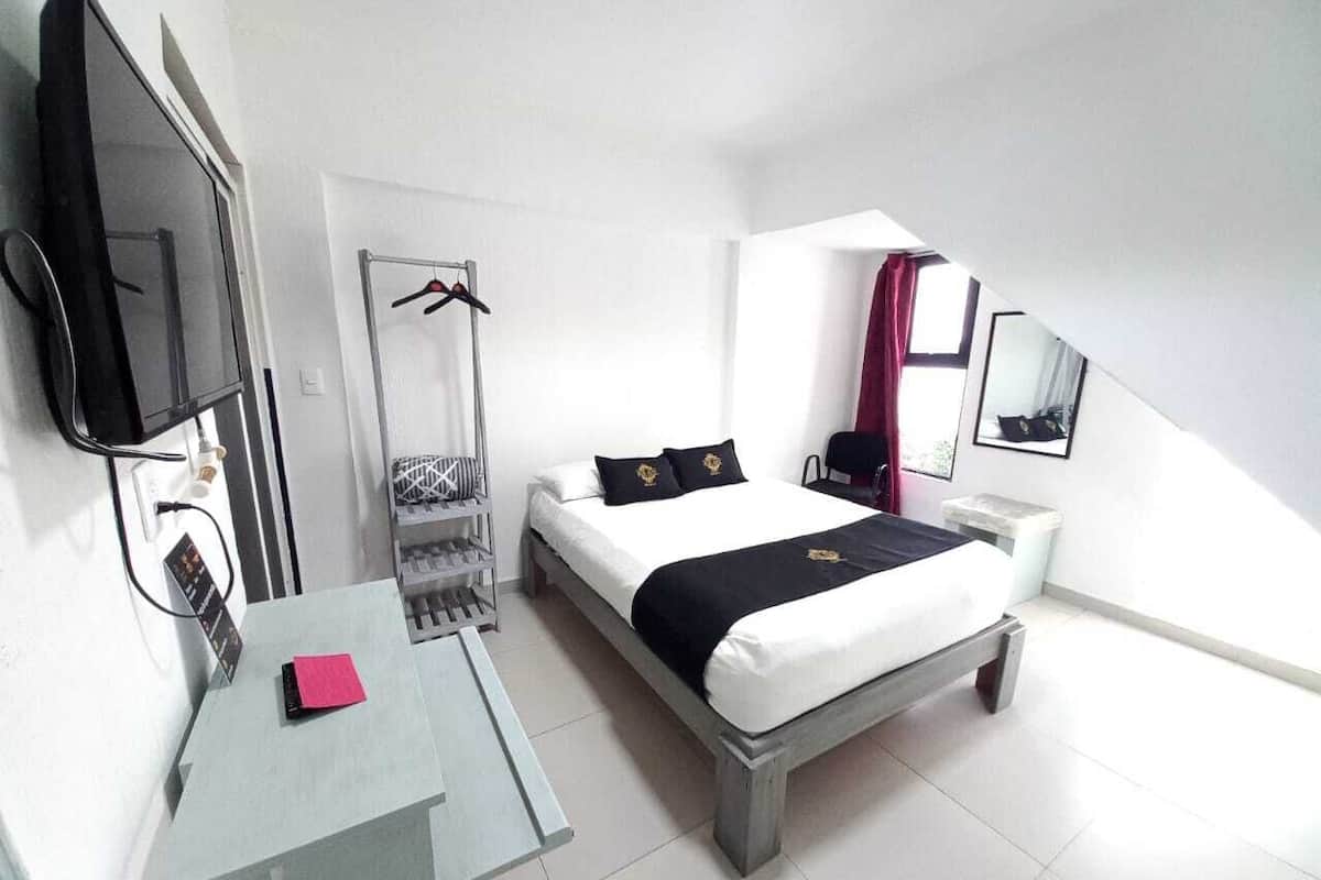 A modern hotel room with a bed, a desk, a TV, a wardrobe, and a window with curtains.